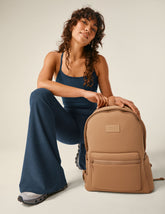 model is wearing a blue slim racerback cropped tank and blue high-waisted flare bottoms with a brown dagne dover backpack.